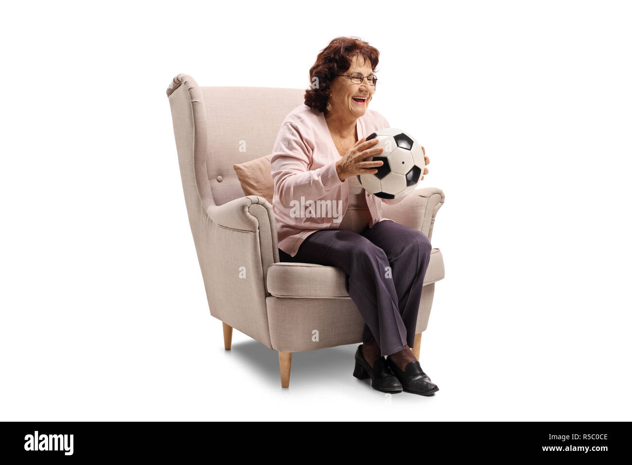 Allegro anziani donna seduta in una poltrona con pallone da calcio isolati su sfondo bianco Foto Stock