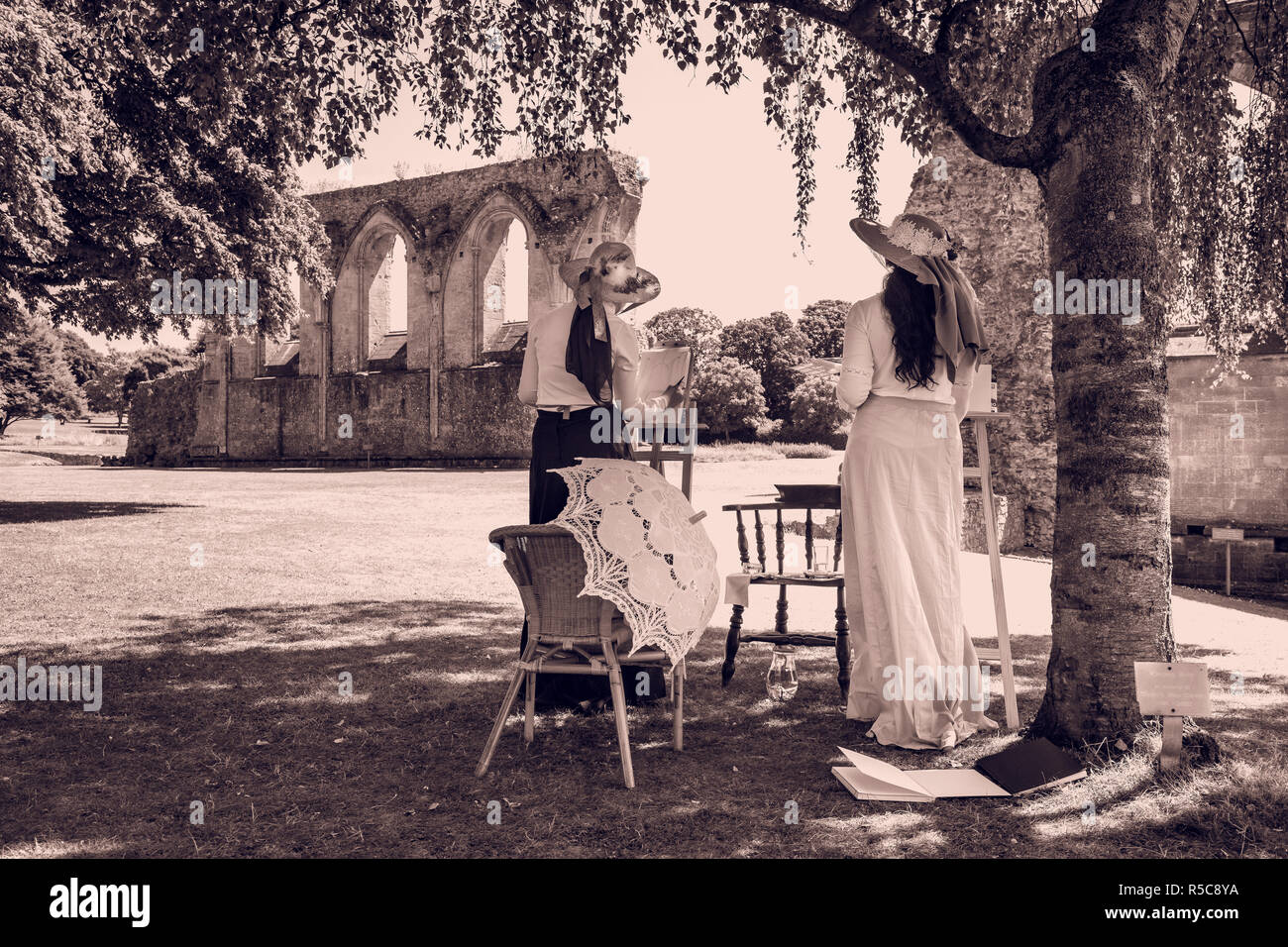 Due giovani donne nel periodo edoardiano costumi posano con i loro cavalletti su una giornata d'estate presso la storica abbazia di Glastonbury, Somerset. Foto Stock