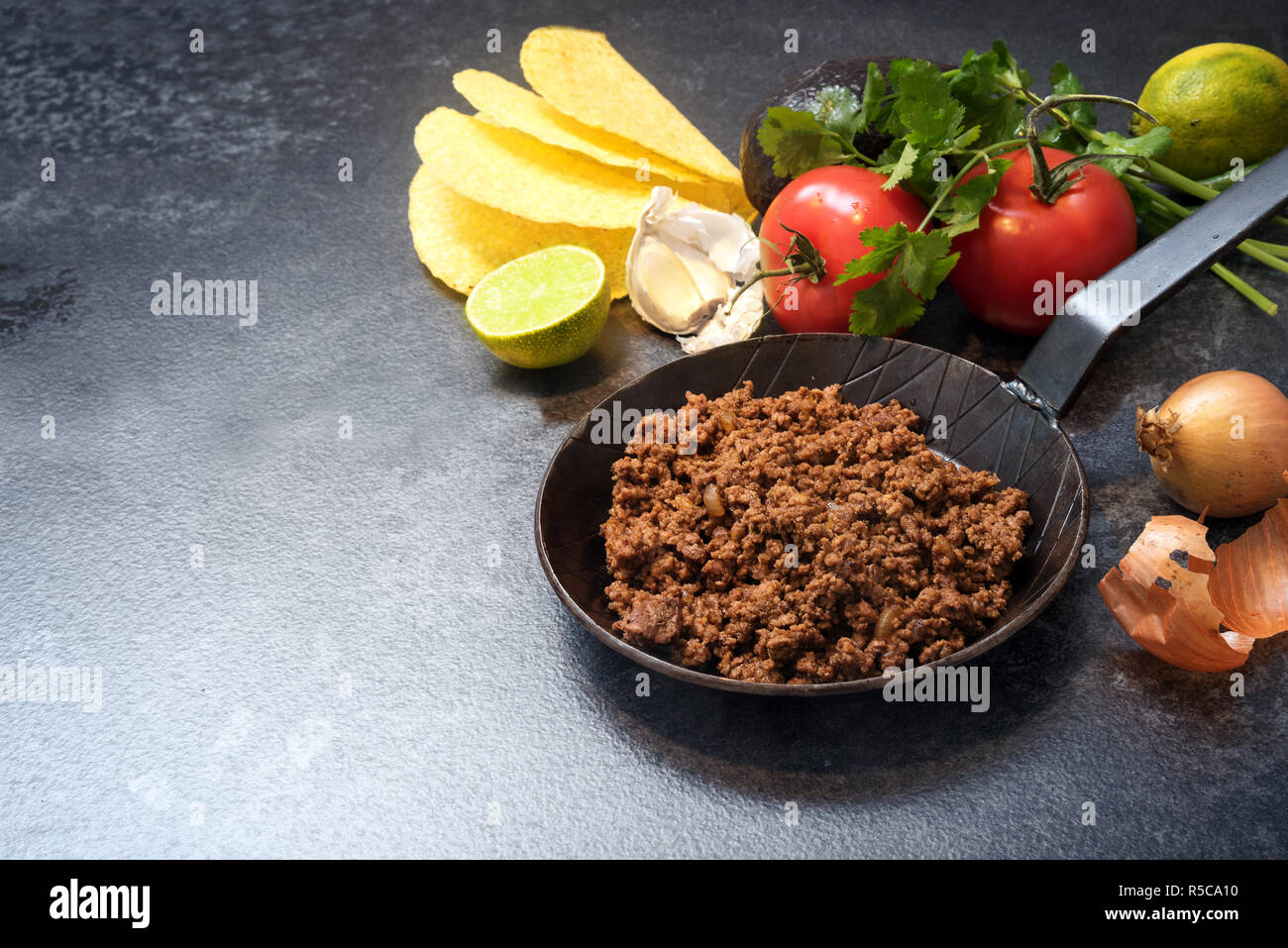 Ingredienti per i tacos con arrosto di manzo in una padella i pomodori, la cipolla, l'aglio, calce, avocado e erbe su una pietra scura con sfondo spazio copia, selecte Foto Stock