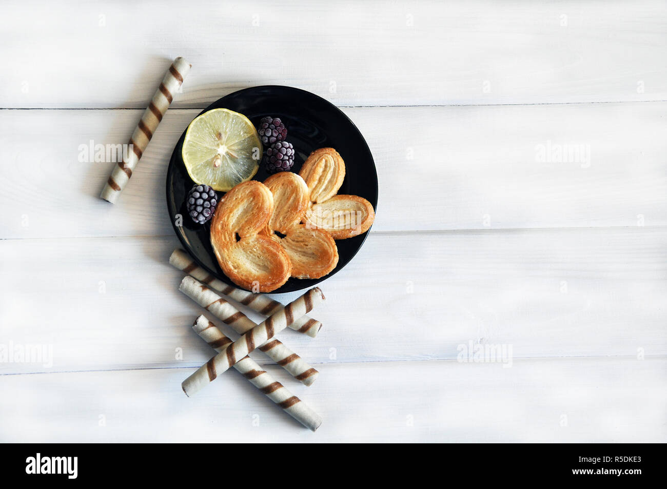 Dolce-personale con fettina di limone e frutti di bosco surgelati sul tondo nero piastra bianca e un tavolo di legno. Foto Stock