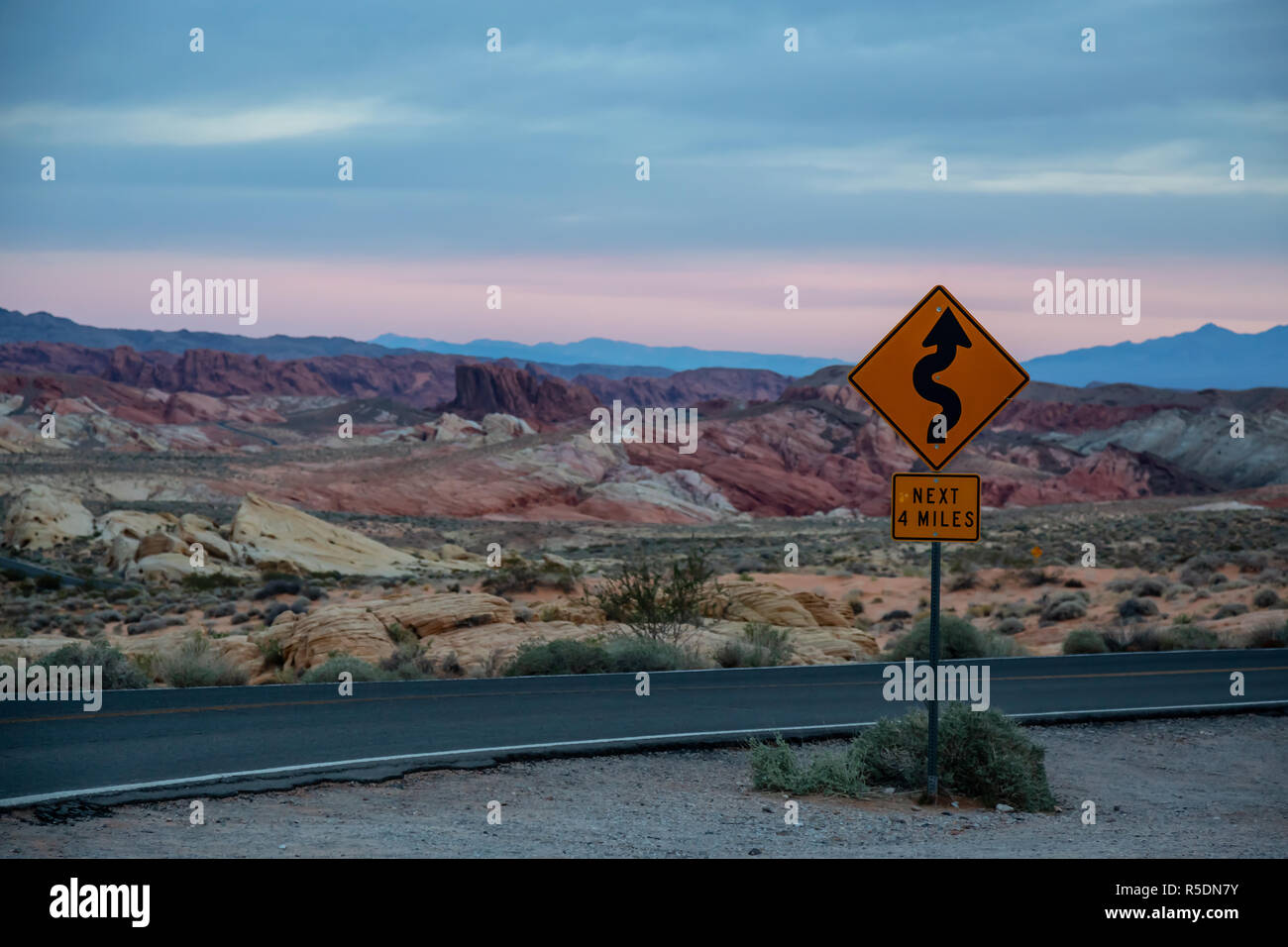 Winding Road Sign su una strada panoramica nel deserto durante una torbida sunrise. Prese nella Valle del Fuoco del parco statale, Nevada, Stati Uniti. Foto Stock
