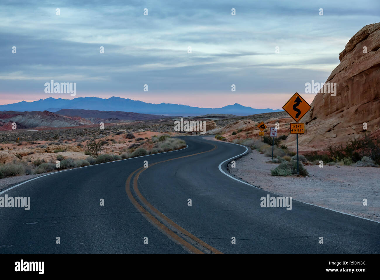 Winding Road Sign su una strada panoramica nel deserto durante una torbida sunrise. Prese nella Valle del Fuoco del parco statale, Nevada, Stati Uniti. Foto Stock