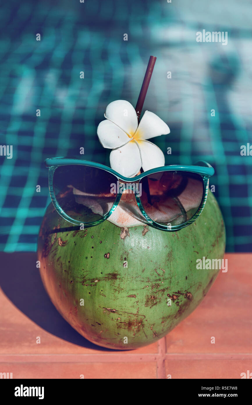 Fresco di succo di cocco con paglia, fiore e gli occhiali da sole sul bordo di una piscina - vacanza concetto tropicale Foto Stock