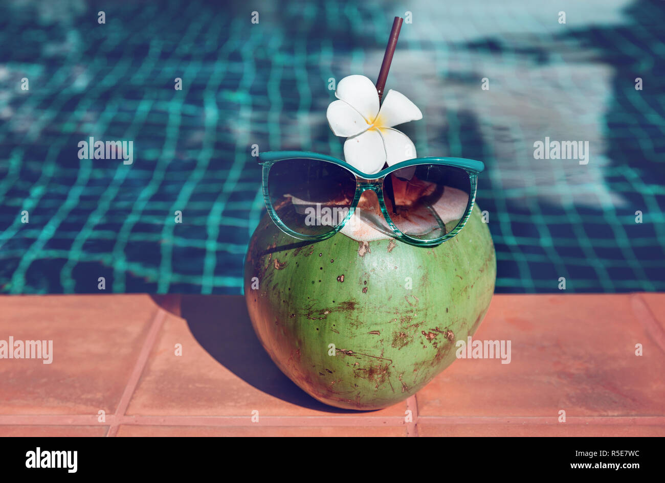Fresco di succo di cocco con paglia, fiore e gli occhiali da sole sul bordo di una piscina - vacanza concetto tropicale Foto Stock