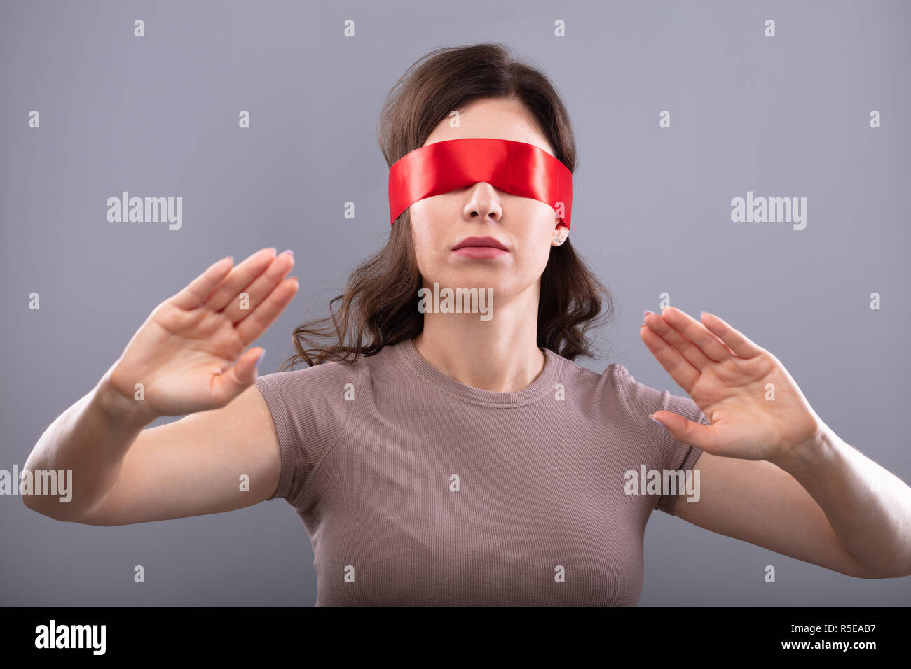 Giovane donna con gli occhi coperti con nastro rosso su sfondo grigio Foto Stock