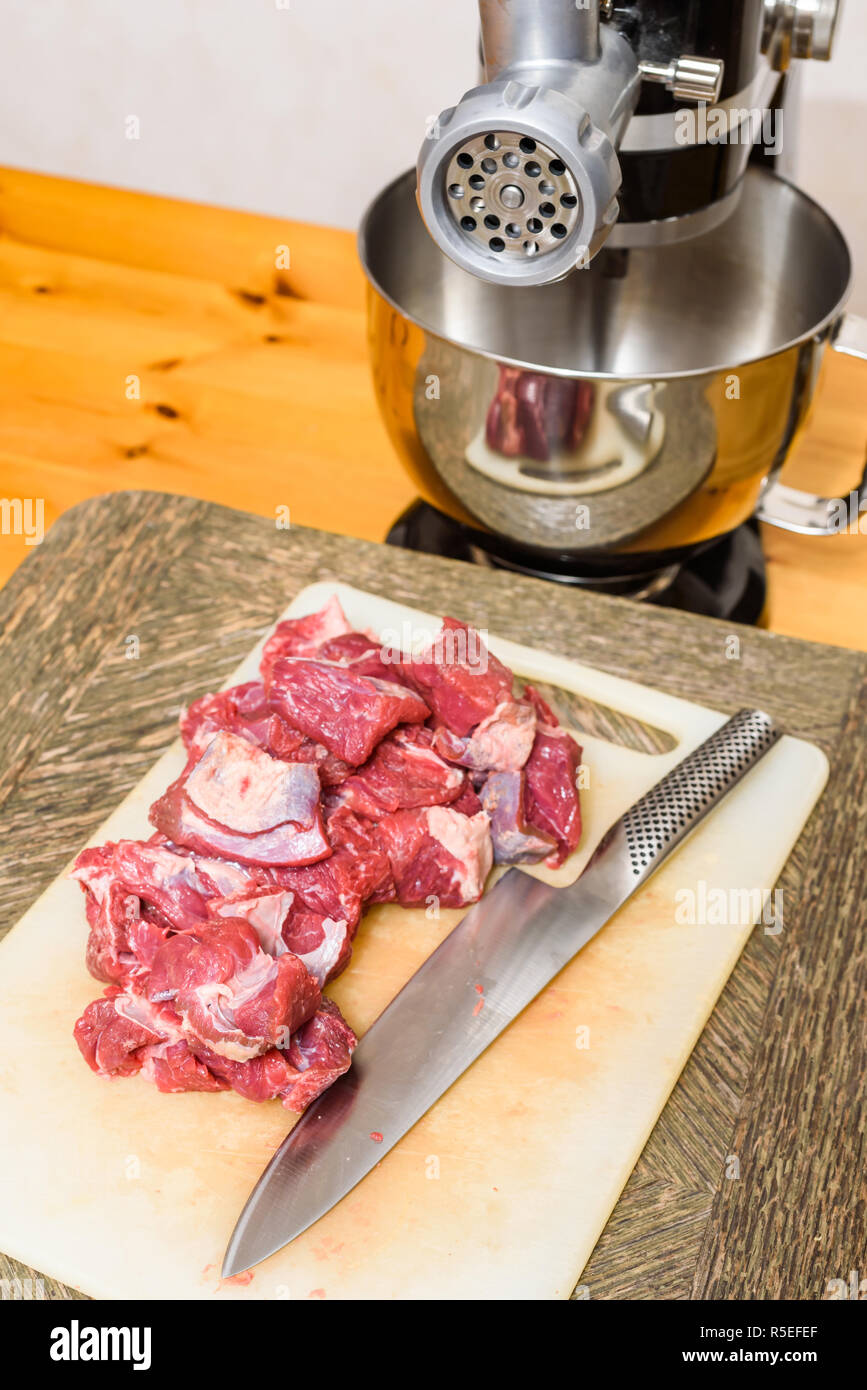 Pila di tagliare la carne cruda (chuck parte) e il coltello sul tagliere con il tritacarne in retro. Foto Stock