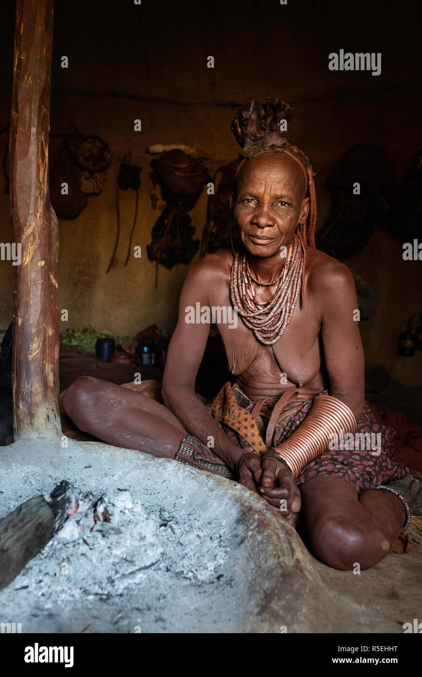 Ritratto di un vecchio Himba donna seduta sul terreno del suo rifugio accanto al fuoco. Foto Stock