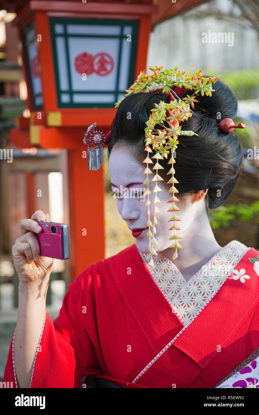 Giappone, Kyoto, Gion, Maiko (apprendista geisha) vestita in kimono prendendo foto sul telefono cellulare Foto Stock