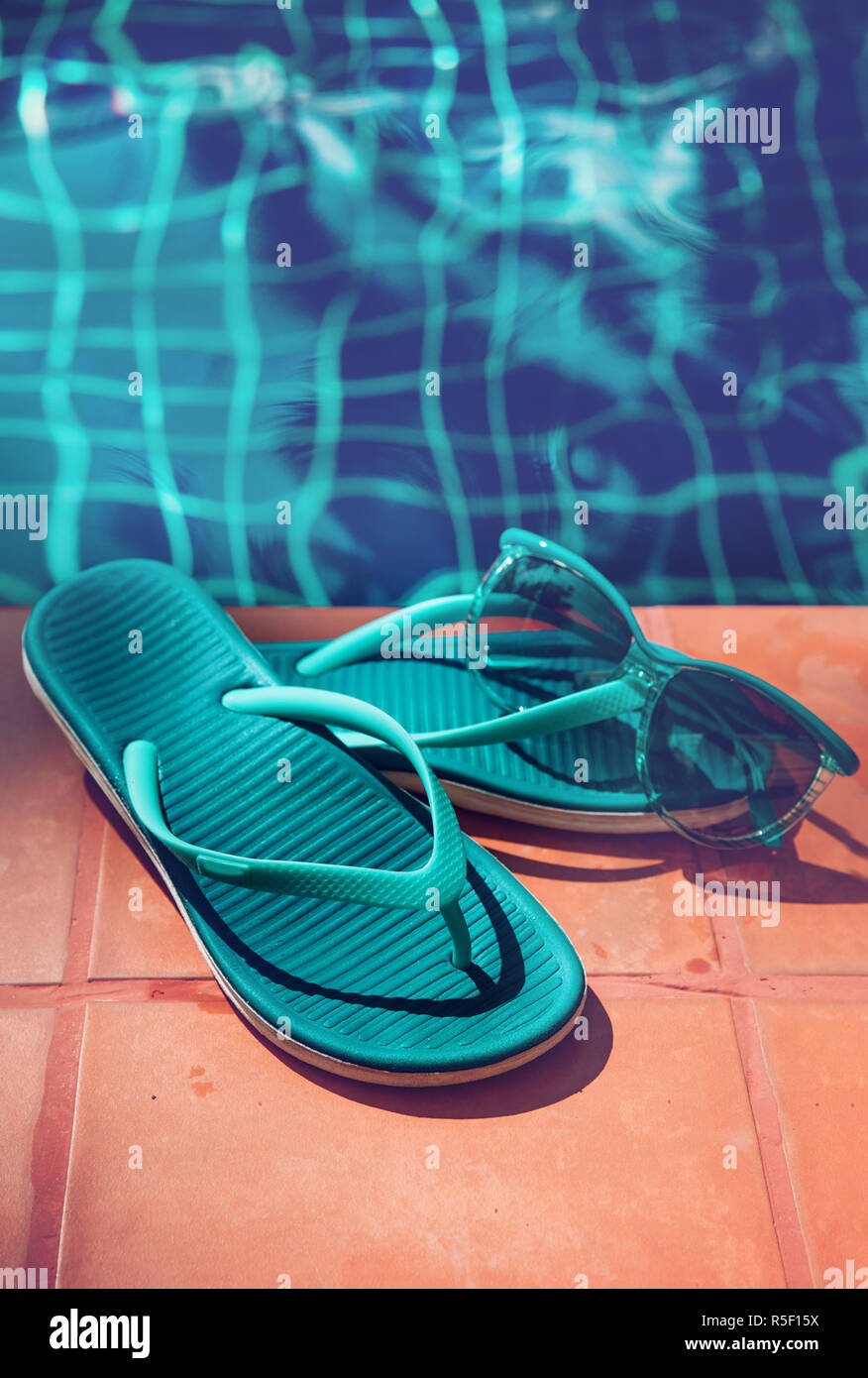 Pantofole blu e gli occhiali da sole sul bordo di una piscina - vacanza concetto tropicale Foto Stock
