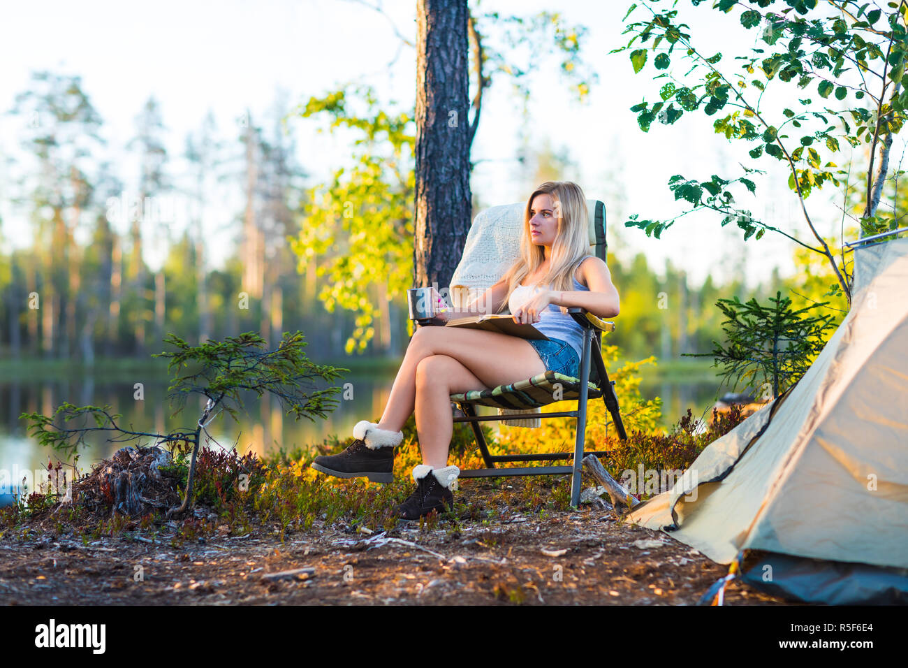 Giovane donna bionda in camping vicino al lago di lettura di un libro Foto Stock