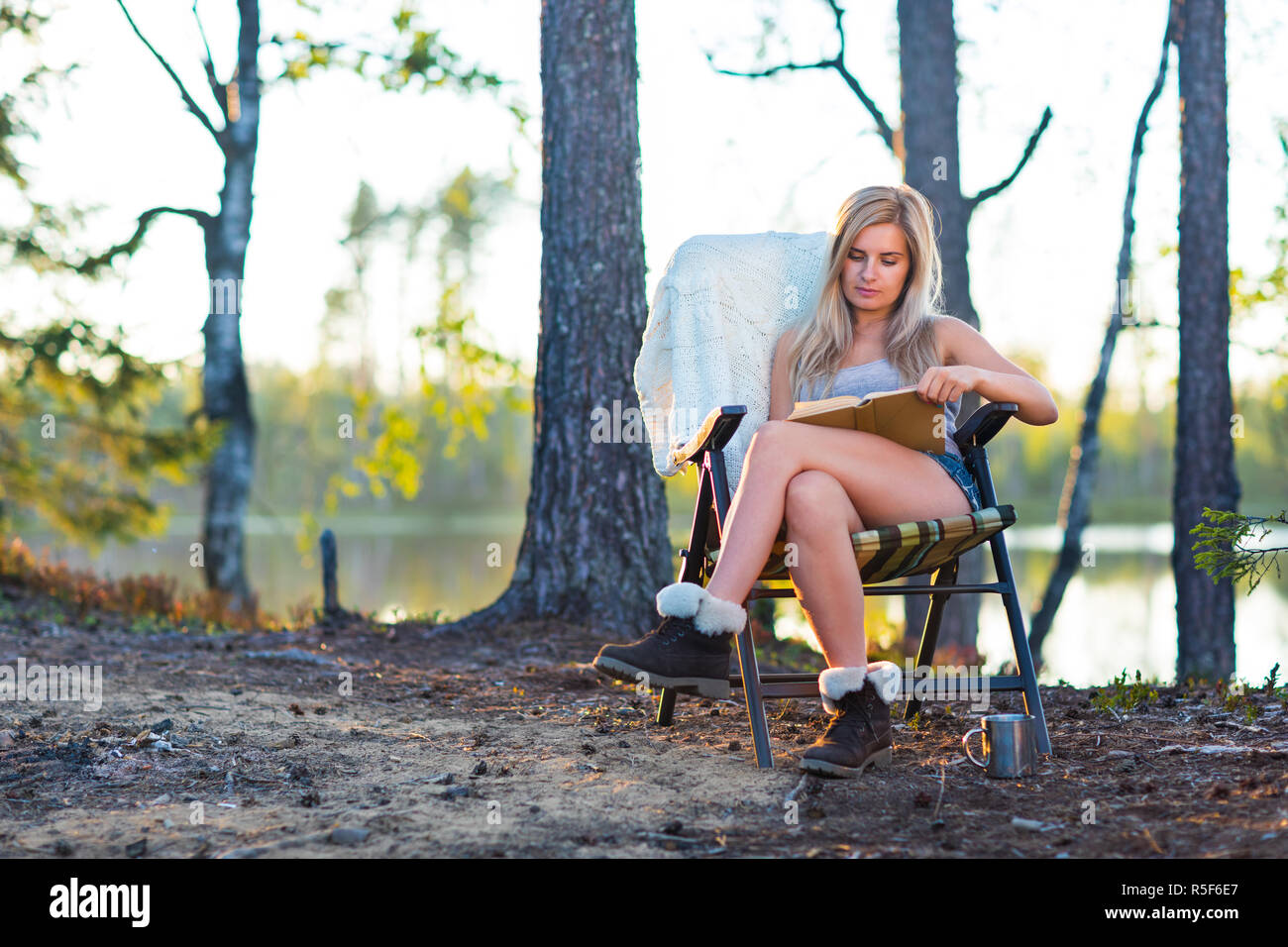 Giovane donna bionda in camping vicino al lago di lettura di un libro Foto Stock