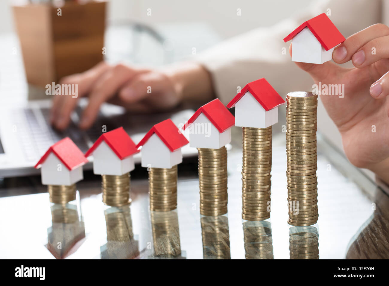 Case in miniatura sopra la pila di monete sul tavolo di legno Foto Stock
