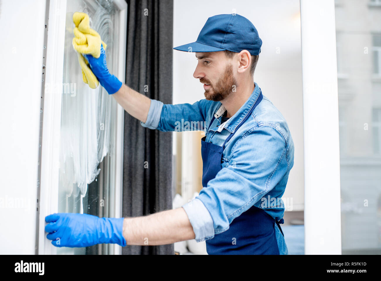 L'uomo come un pulitore professionale in uniforme blu nella finestra di lavaggio con cotone interni del tergicristallo Foto Stock