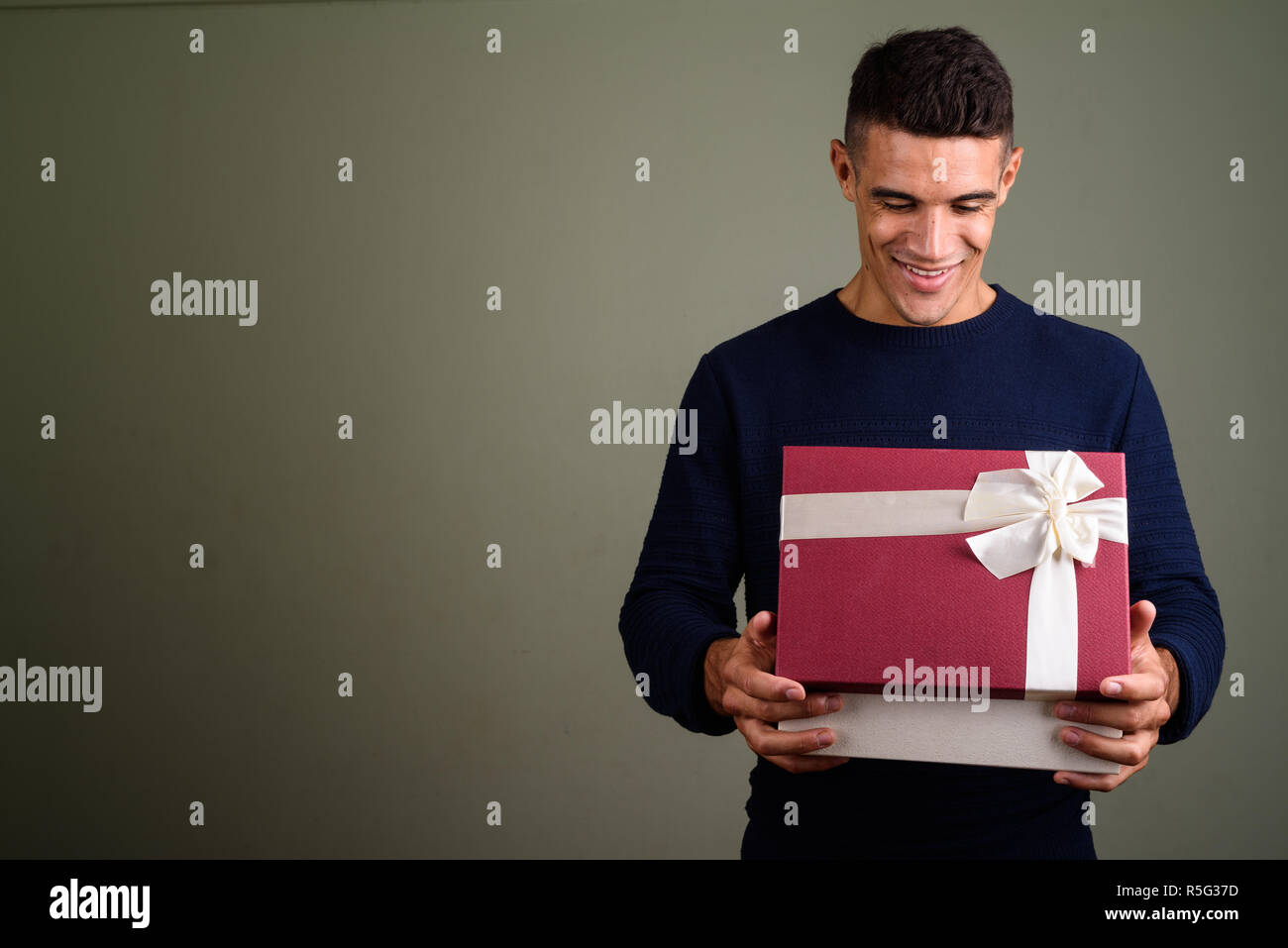 Giovane uomo bello azienda confezione regalo contro sfondo colorato Foto Stock