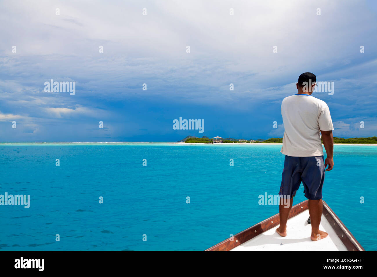 Venezuela, Arcipelago di Los Roques PARCO NAZIONALE, Noronquises Isola, Skipper permanente sulla parte anteriore della barca alla ricerca di tartarughe di mare Foto Stock