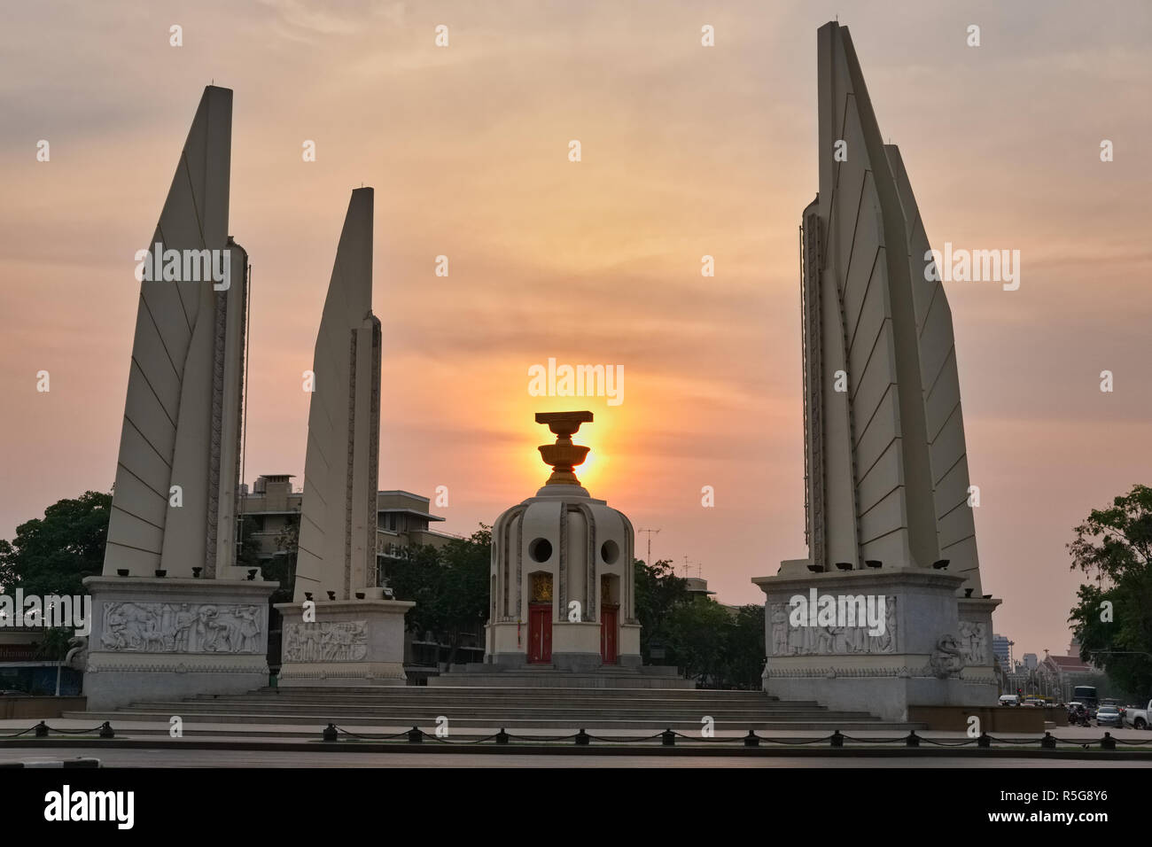 La democrazia è un monumento a Bangkok, Thailandia, il sole di setting posizionato in corrispondenza del suo centro, dove una rappresentazione simbolica della costituzione tailandese è in primo piano Foto Stock