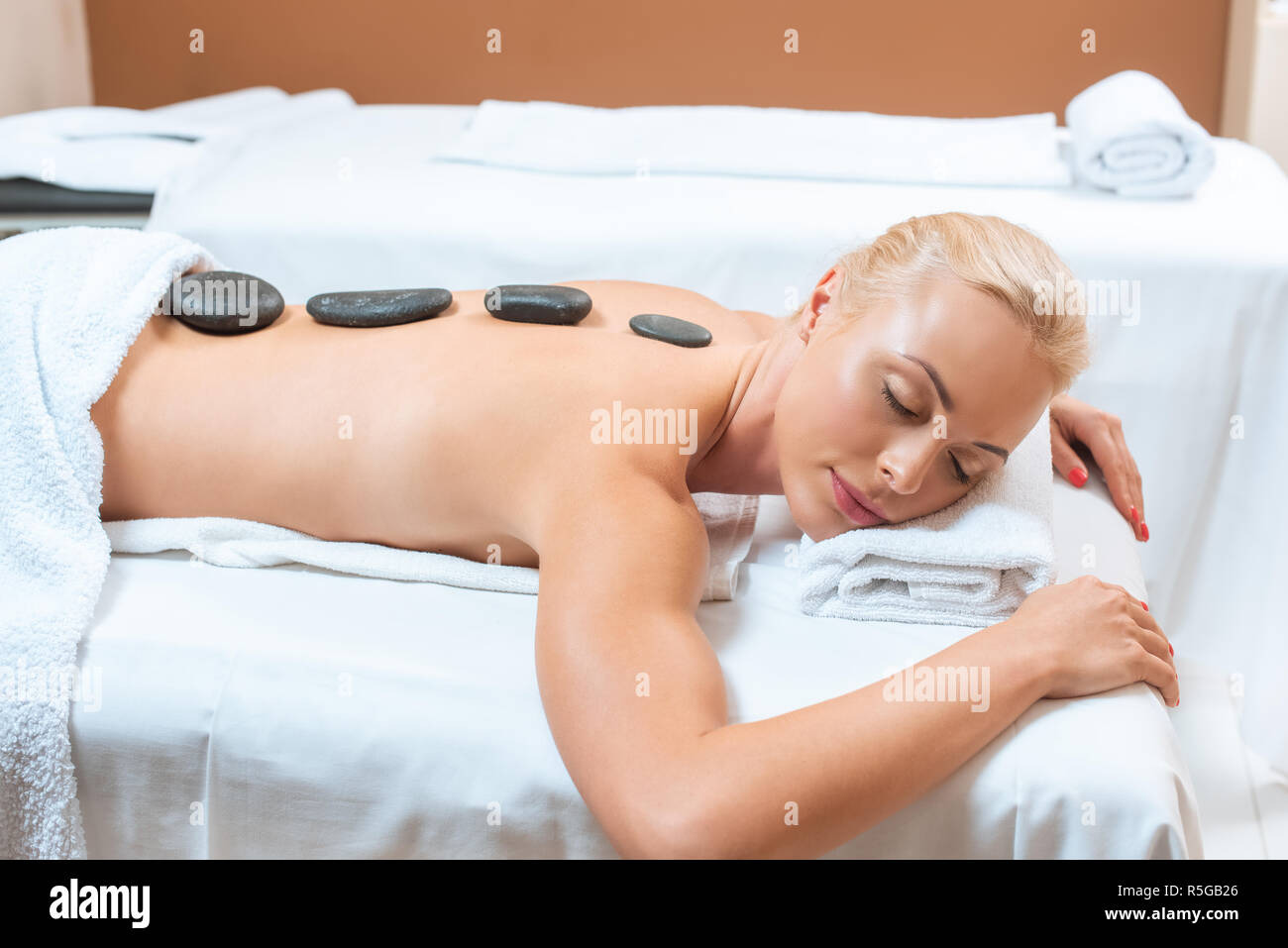 Donna sdraiata sul lettino da massaggio con pietre calde sul retro Foto Stock