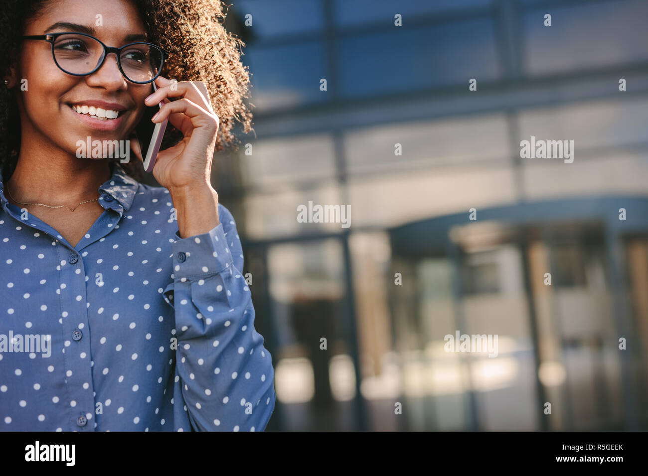 Donna africana in camicia di parlare al telefono e sorridente all'esterno. Close up di felice giovane femmina facendo una telefonata mentre in piedi fuori con copia sp Foto Stock
