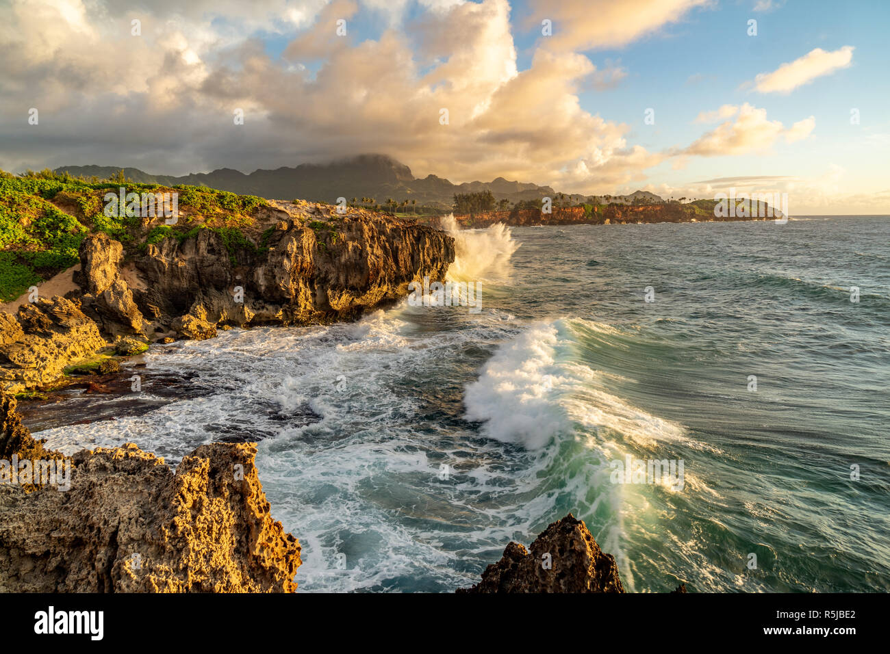 Onde che si infrangono in Makawehi Bluff durante la calda luce alba illumina le nuvole, Kauai, Hawaii Foto Stock
