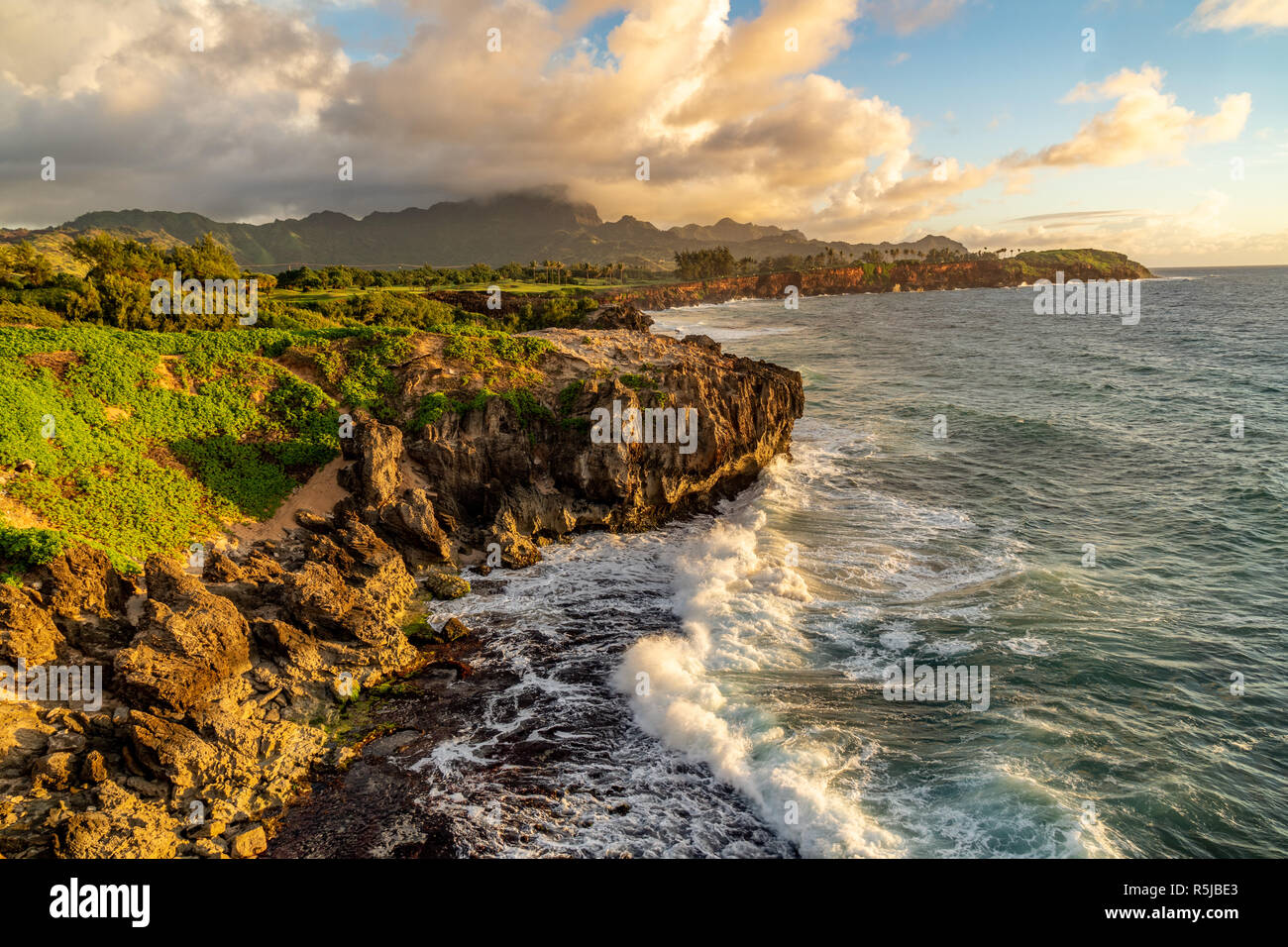 Onde che si infrangono in Makawehi Bluff durante la calda luce alba illumina le nuvole, Kauai, Hawaii Foto Stock