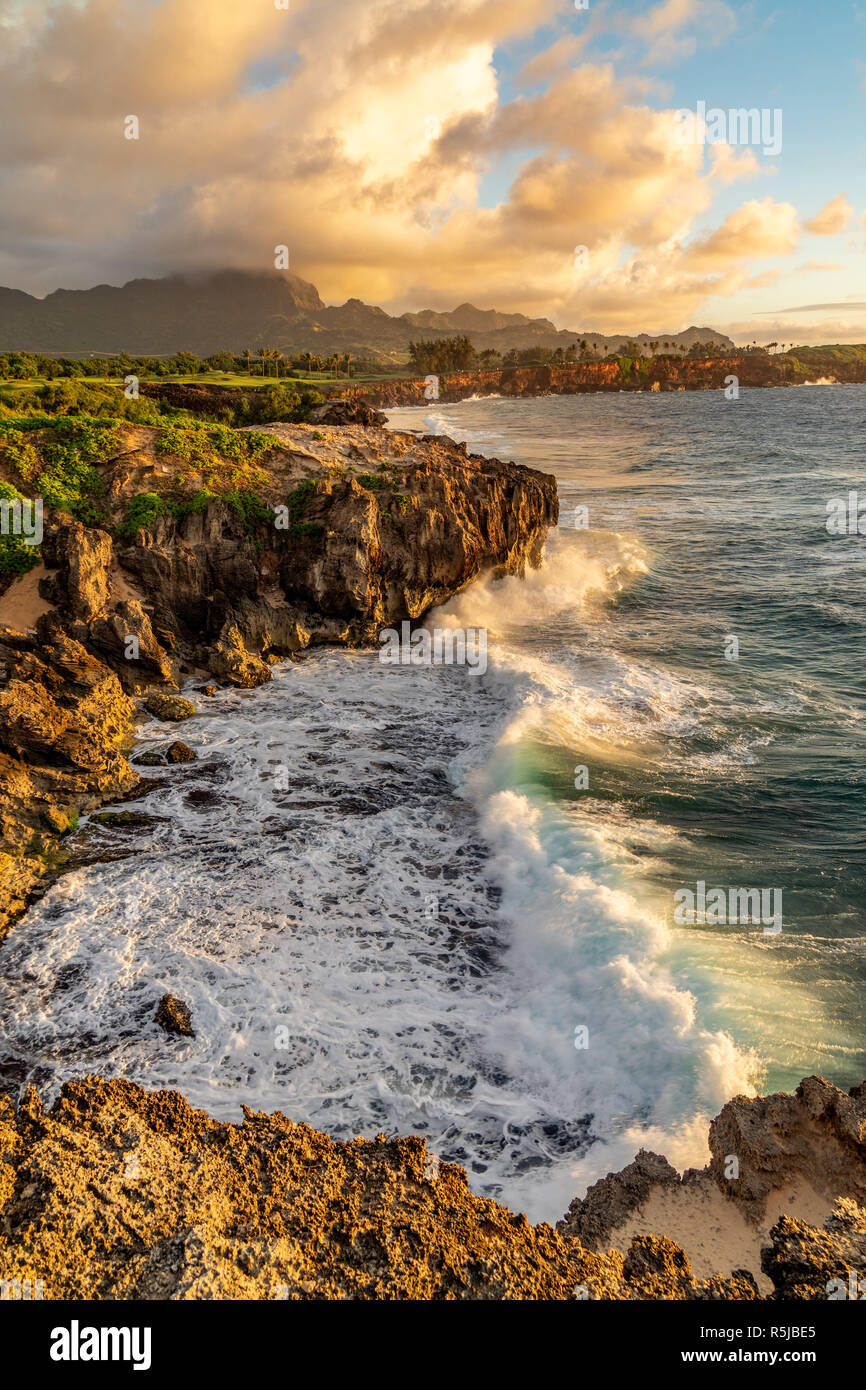 Onde che si infrangono in Makawehi Bluff durante la calda luce alba illumina le nuvole, Kauai, Hawaii Foto Stock