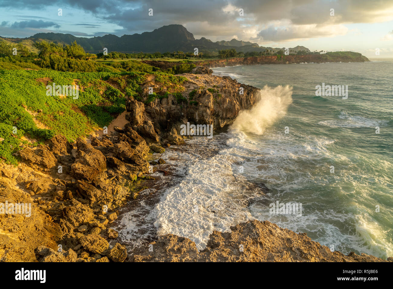 Onde che si infrangono in Makawehi Bluff durante la calda luce alba illumina le nuvole, Kauai, Hawaii Foto Stock