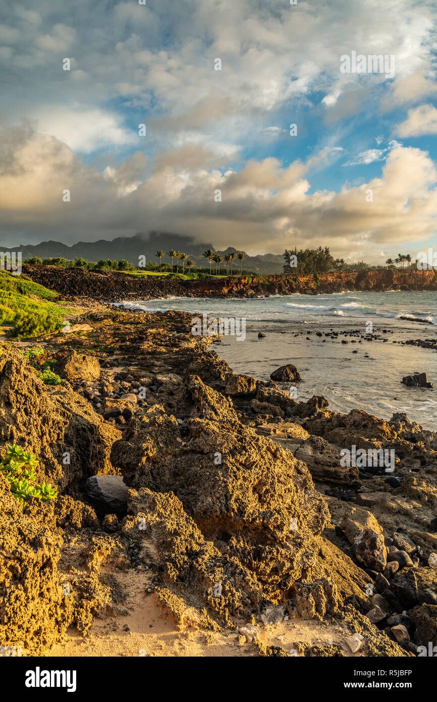 Onde che si infrangono in Makawehi Bluff durante la calda luce alba illumina le nuvole, Kauai, Hawaii Foto Stock