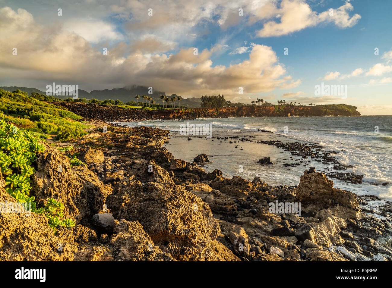 Onde che si infrangono in Makawehi Bluff durante la calda luce alba illumina le nuvole, Kauai, Hawaii Foto Stock