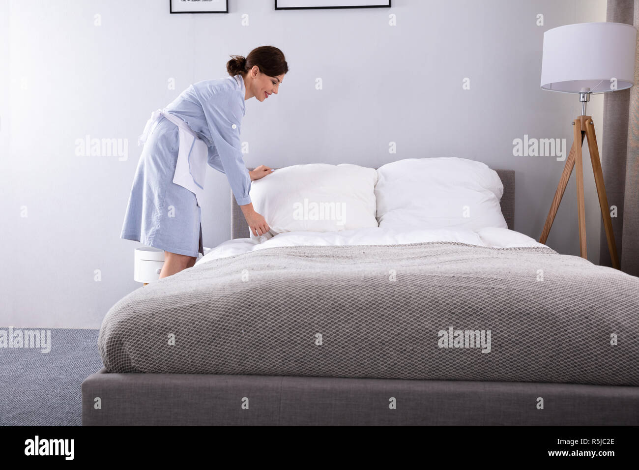 Donna sorridente governante rendendo letto in camera in hotel Foto Stock