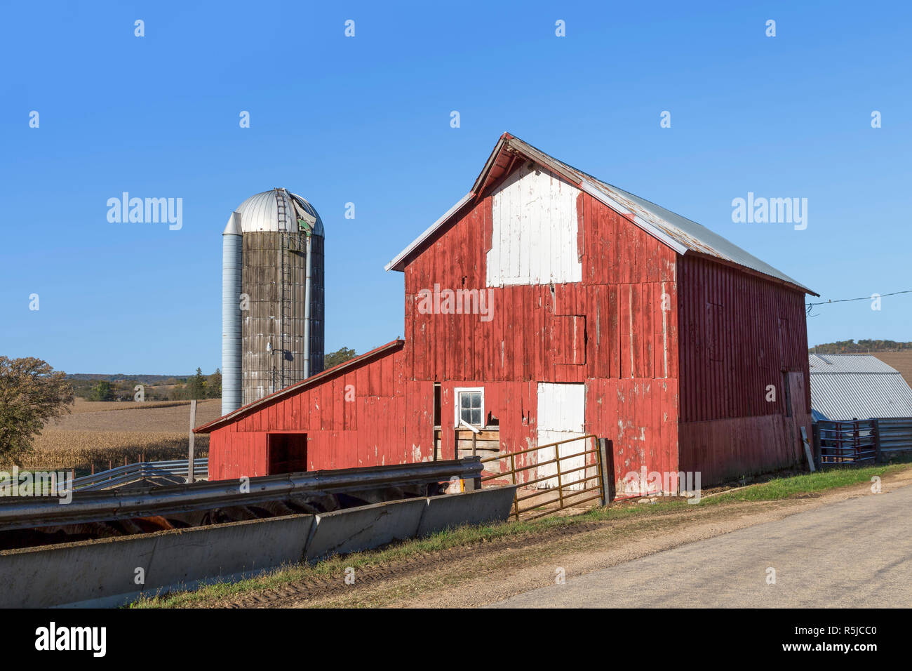 Un vecchio colore rosso brillante granaio e silo stand lungo la strada in una zona rurale Illinois farm. Foto Stock