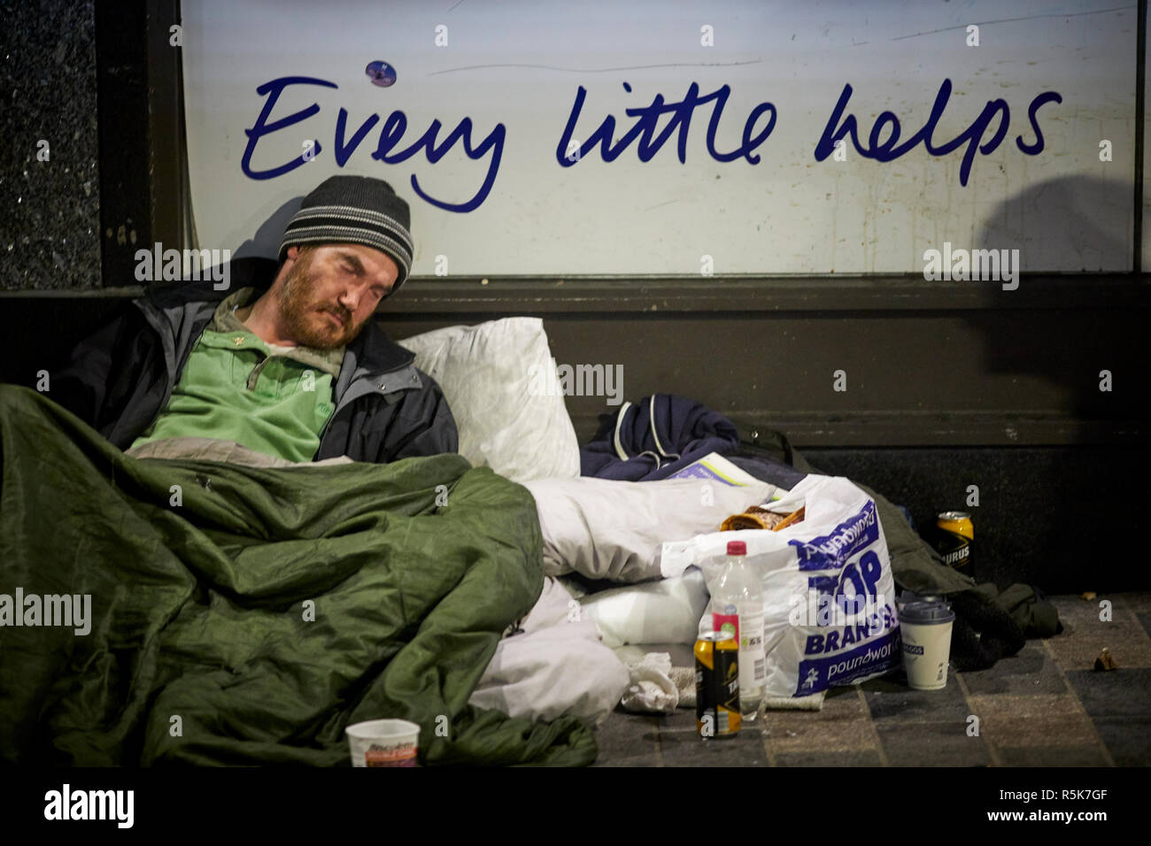 Il centro di Liverpool sleeping senzatetto di accattonaggio uomo con il disordine intorno a lui come egli dorme, ogni piccolo aiuta a tesco slogan Foto Stock