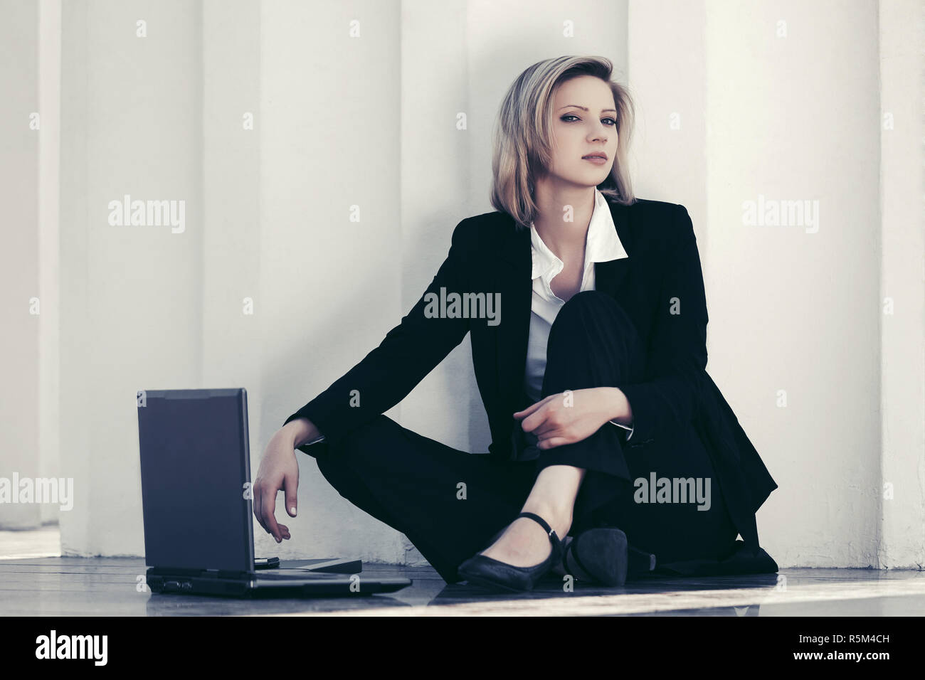 Giovane donna di affari con computer portatile seduto alla parete elegante modello di moda in costume nero per esterno Foto Stock