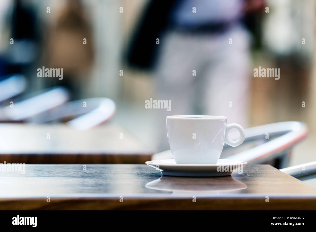 Una tazza di caffè espresso su di un tavolo di legno aperto con persone in background. Foto Stock