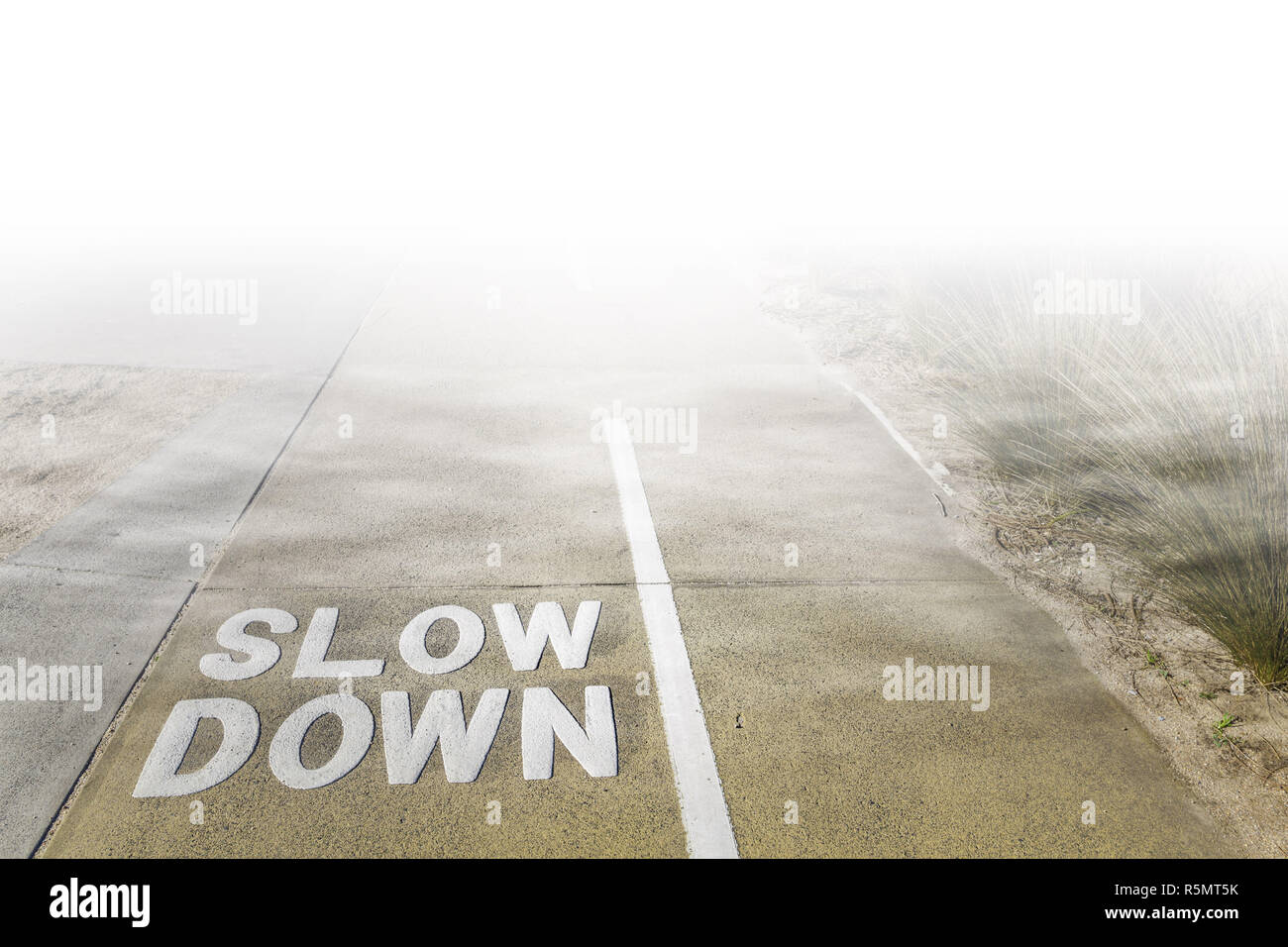 Rallentare il segno scritto sul sentiero condiviso per i ciclisti e i pedoni vanishing sotto nuvole basse e nebbia Foto Stock