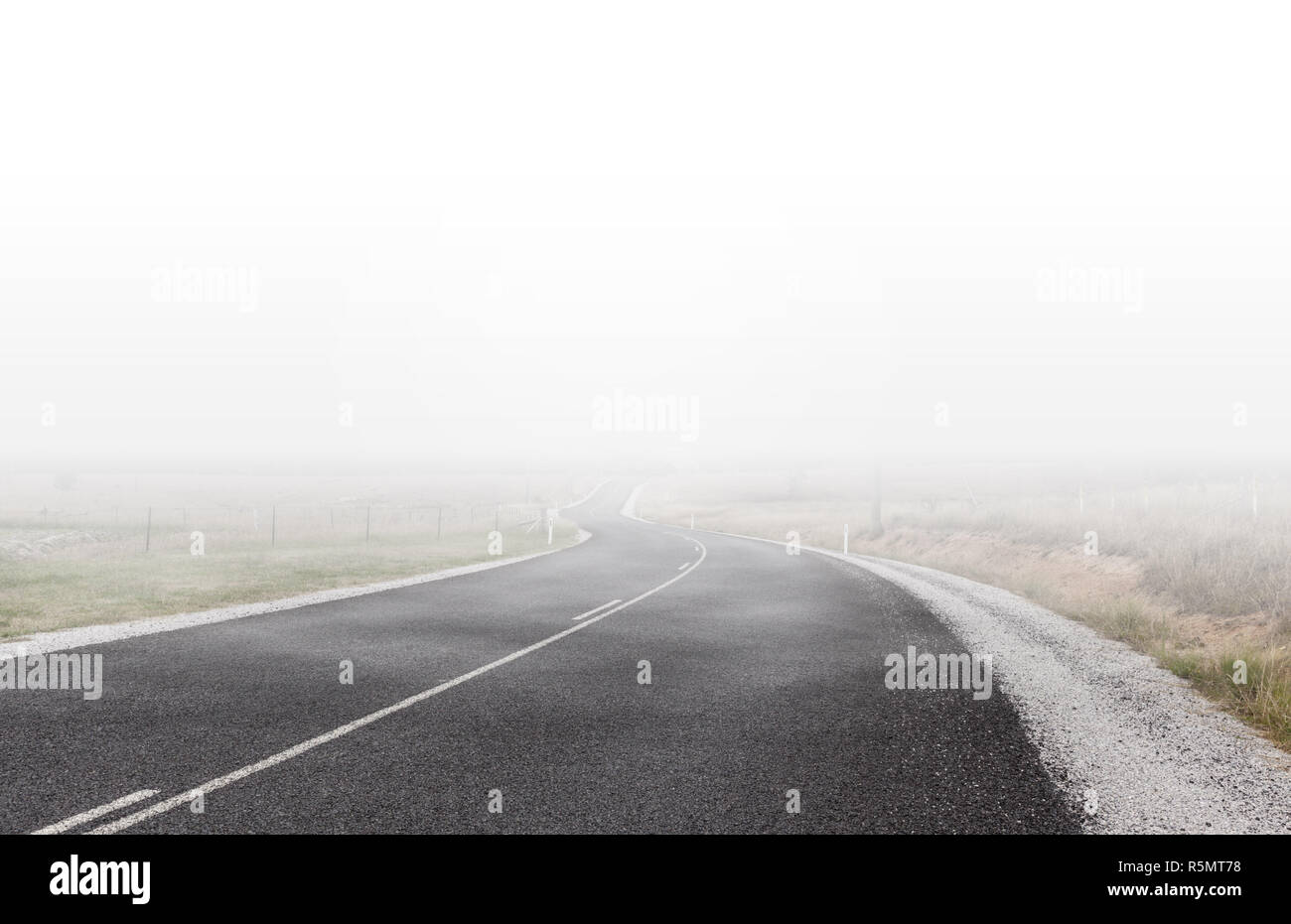 Avvolgimento strada rurale scomparendo in lontananza sotto nuvole basse e nebbia Foto Stock