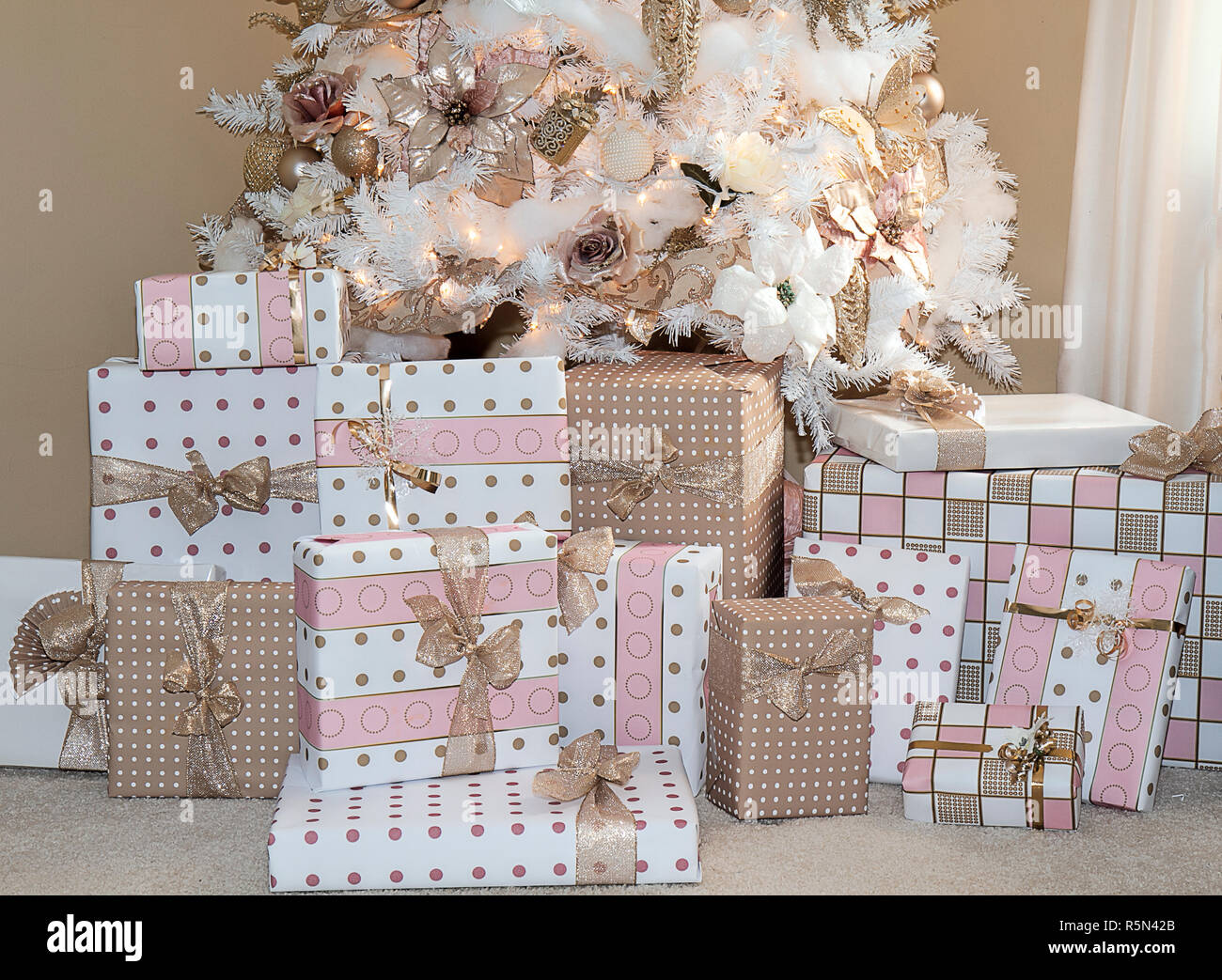 White sognanti albero di Natale nel salotto di casa decorata in popular rosa pallido ornamenti e doni di seguito in abbinamento carta di avvolgimento. Foto Stock