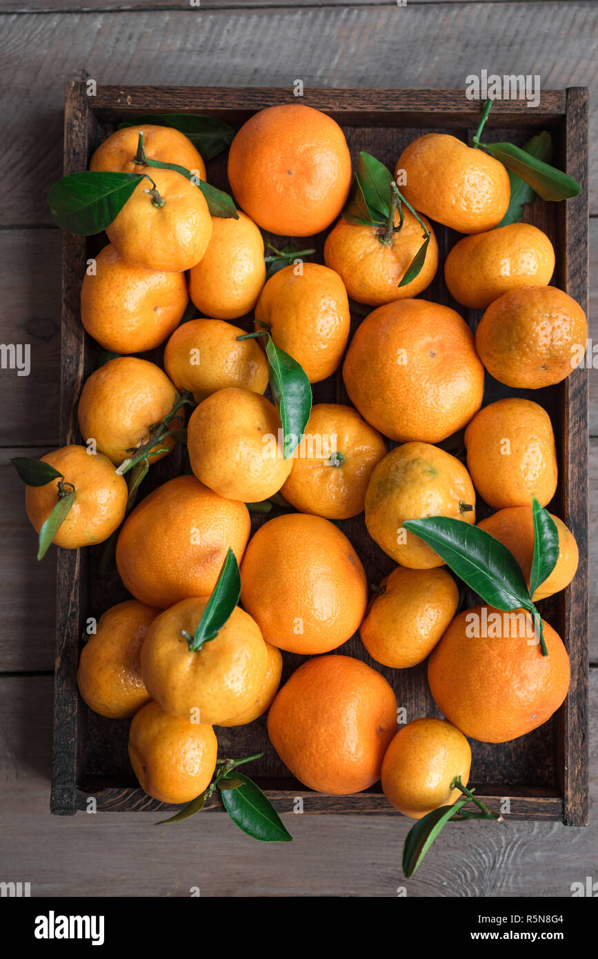 Tangerini (arance, clementine, agrumi) con foglie verdi nella casella su sfondo di legno, vista dall'alto. Foto Stock