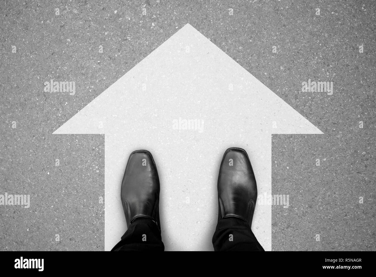 Scarpe nere in piedi sull'asfalto pavimento in cemento bianco e segno di direzione per andare sempre dritto in avanti. Foto Stock