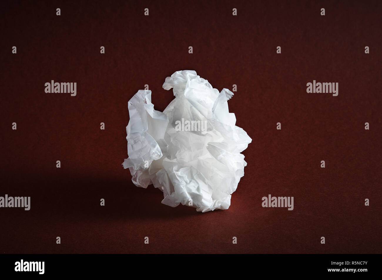 Crumpled white paper sulla texture di sfondo marrone sotto drammatico illuminazione moody Foto Stock