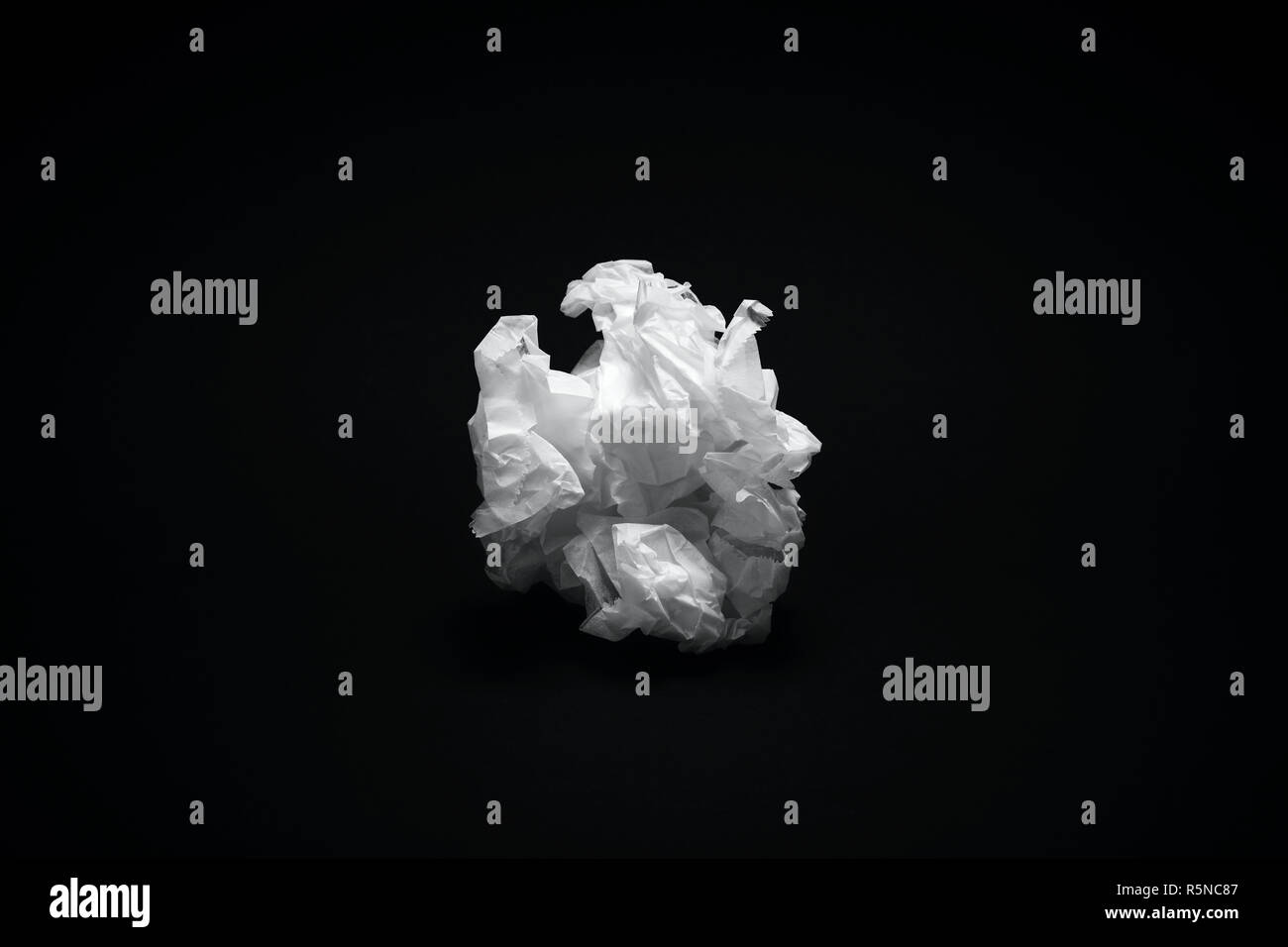 Crumpled white paper texture scuro su sfondo nero sotto il drammatico illuminazione moody Foto Stock