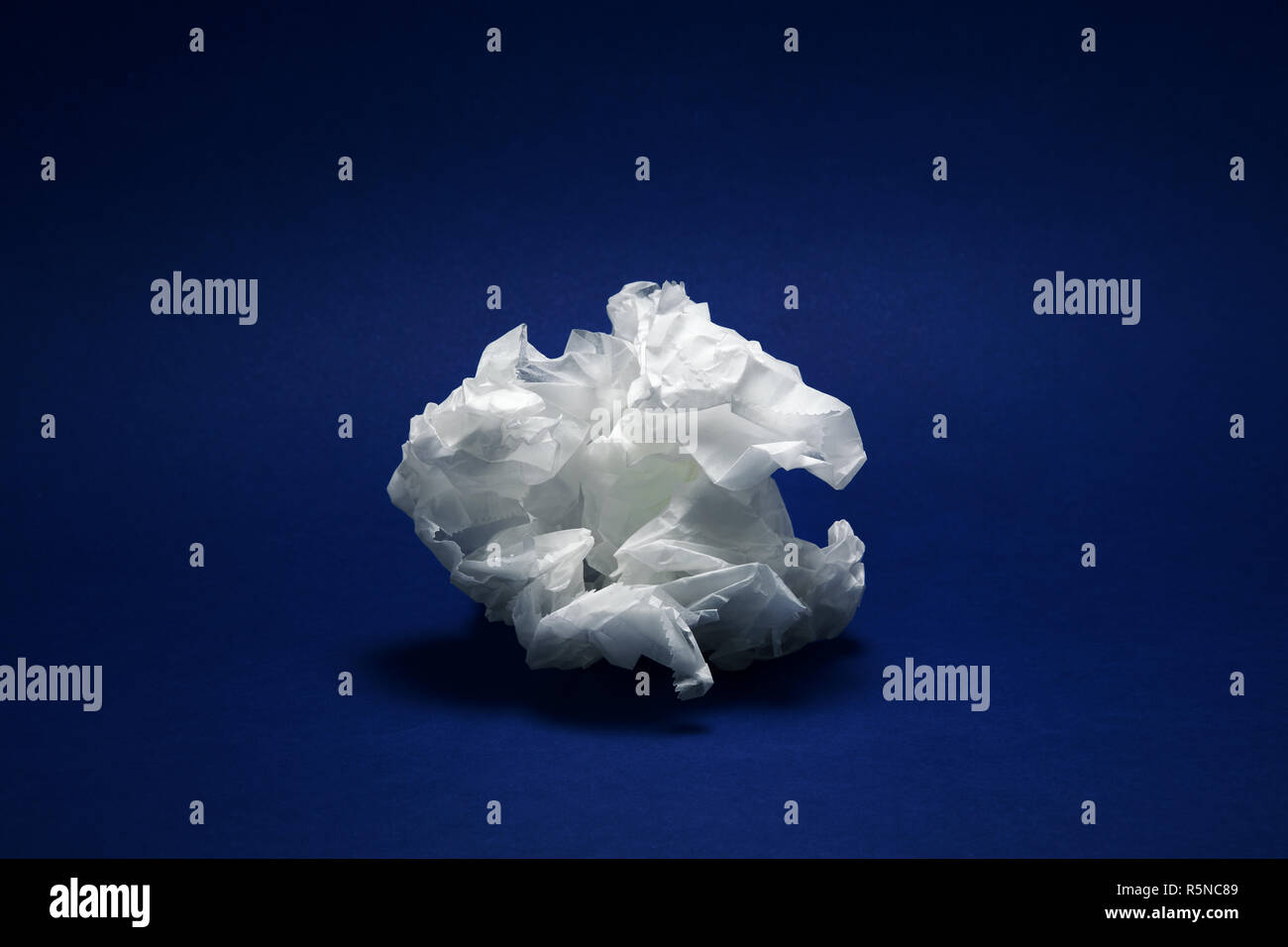 Crumpled white paper texture su sfondo blu scuro sotto drammatico illuminazione moody Foto Stock