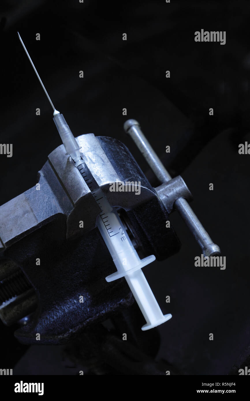 Siringa di cracking all'interno di vecchi vise grip su sfondo scuro con spazio di copia Foto Stock