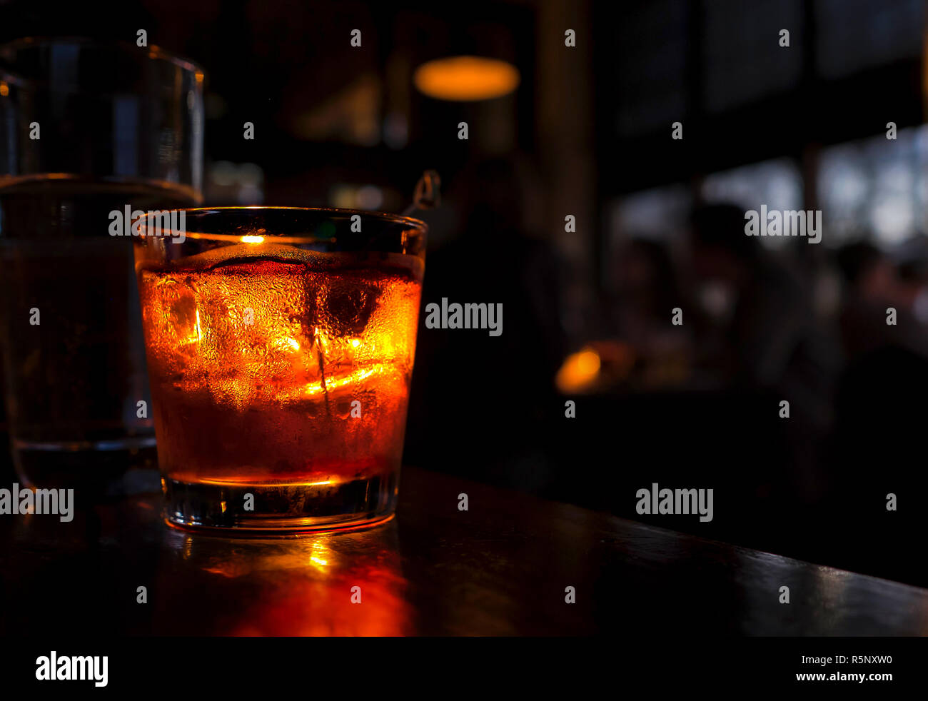Cocktail vicino a un banco di bar. Bere è accesa contro uno sfondo scuro con persone sfocate. Foto Stock