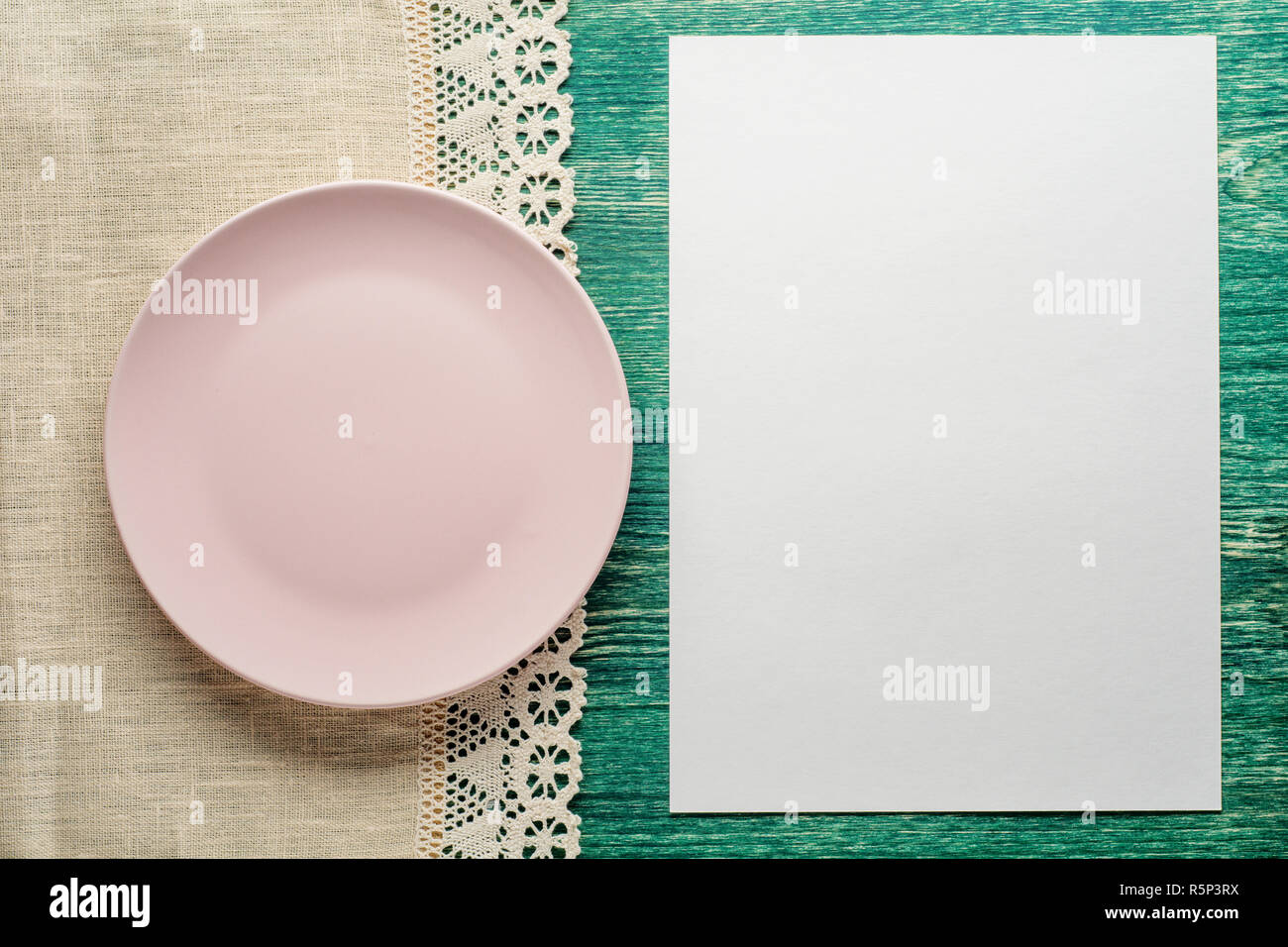Piastra vuota sul tavolo in legno con tovaglia e fogli di carta bianca. Lay piatto. Foto Stock
