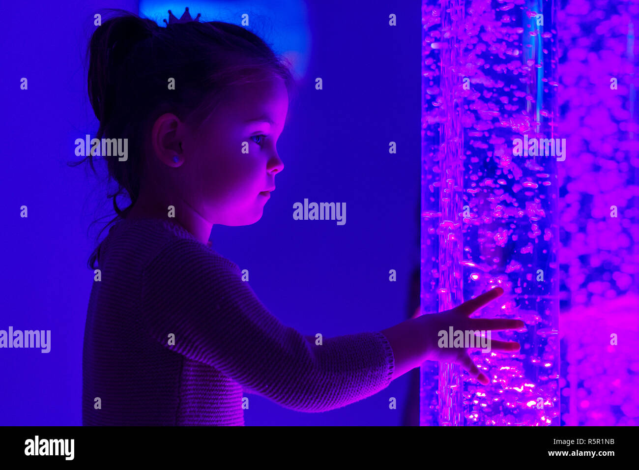 Bambino in terapia di stimolazione sensoriale camera, snoezelen. Bambino interagendo con luci colorate bolle lampada tubo durante la sessione di terapia. Foto Stock