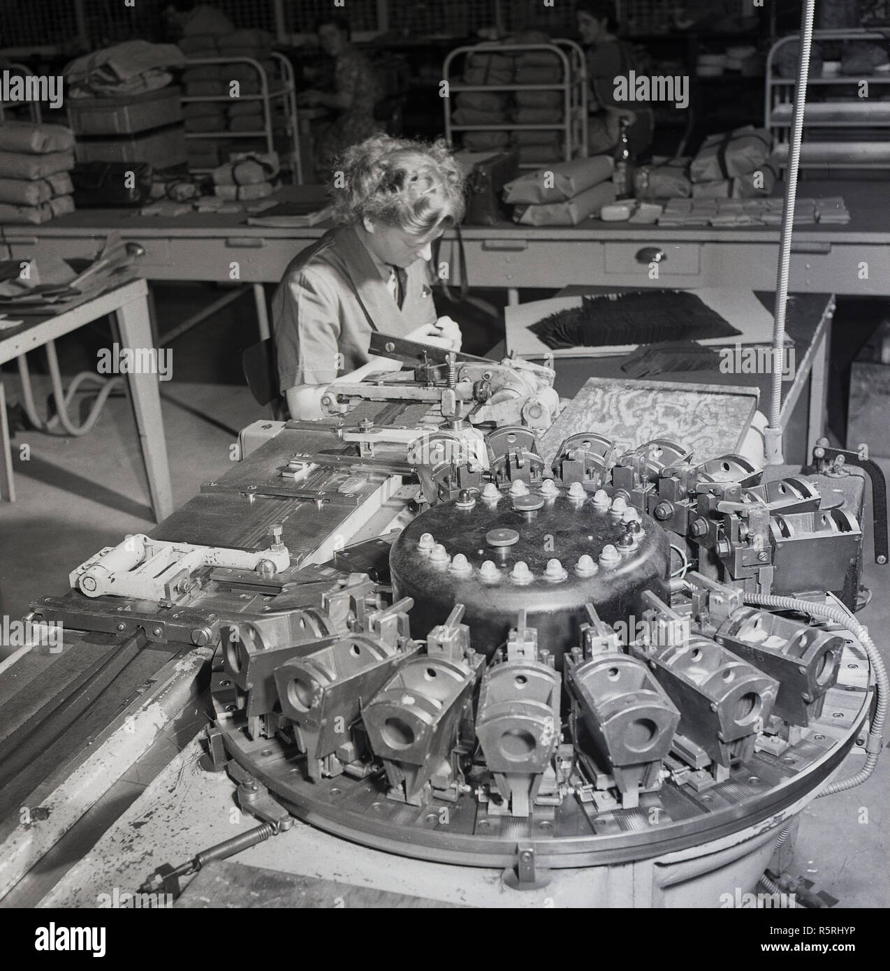 Degli anni Cinquanta, storico, una donna che lavora in una fabbrica industriale, seduto accanto a macchinari, Inghilterra, Regno Unito. Foto Stock