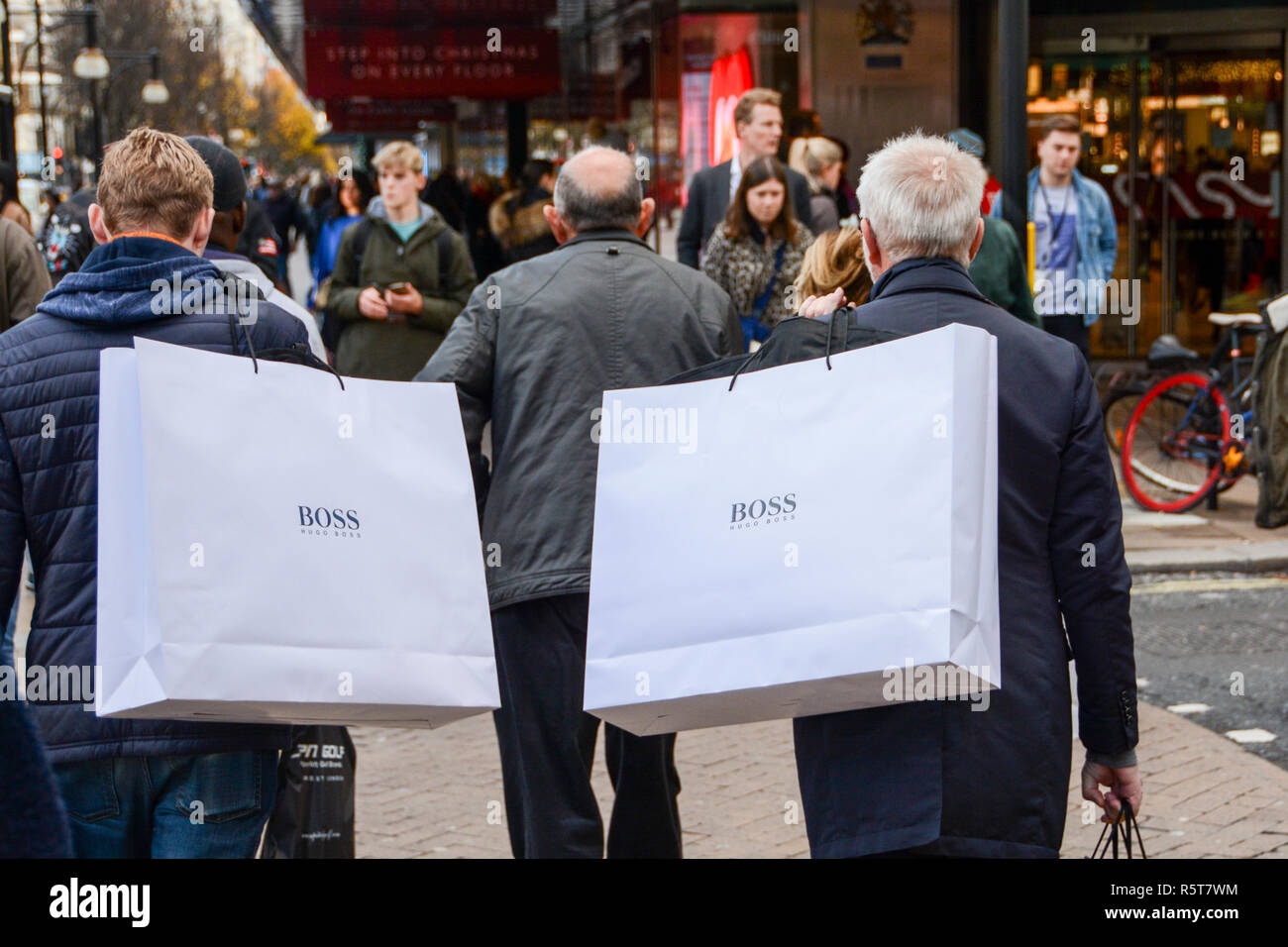 Due acquirenti maschio su una trafficata Oxford Street che trasportano grandi Hugo Boss supporto di carta sacchetti sulle loro spalle Foto Stock