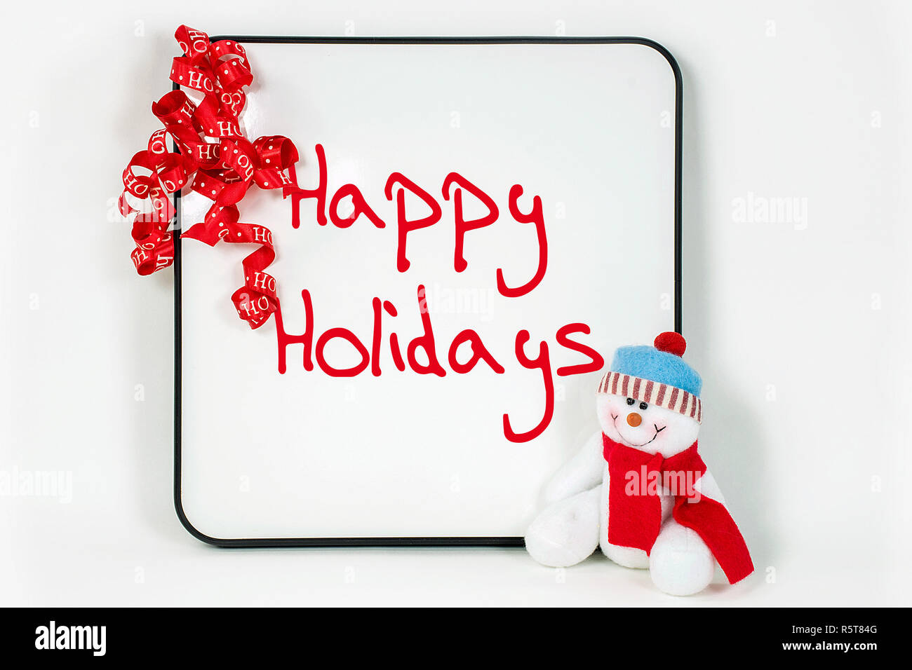 Vacanze felici segno bianco sulla lavagna cancellabile con un nastro rosso e il pupazzo di neve isolato su bianco Foto Stock