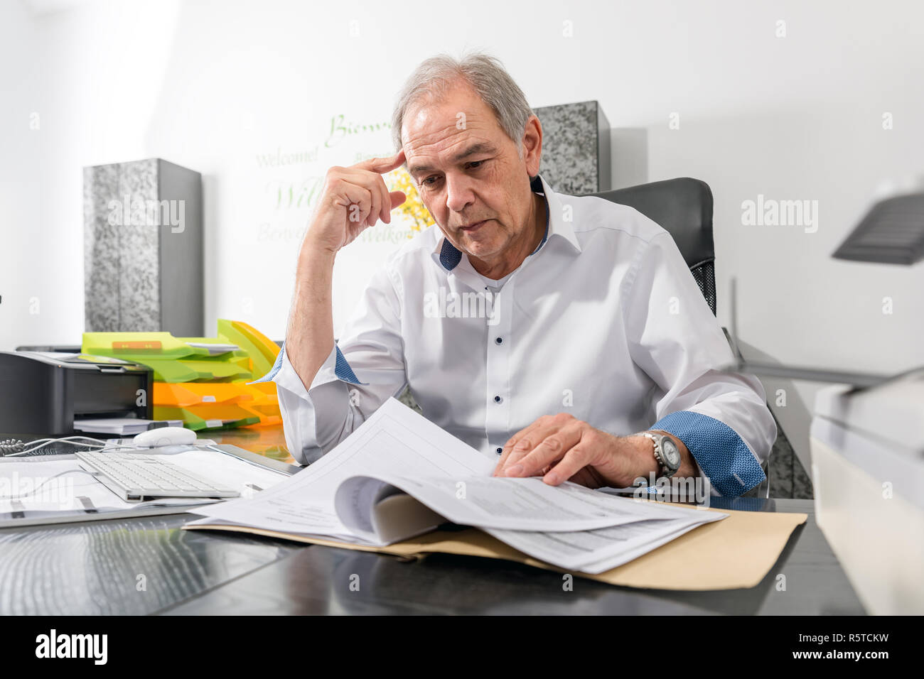 Uomo anziano con camicia bianca si siede a una scrivania Foto Stock