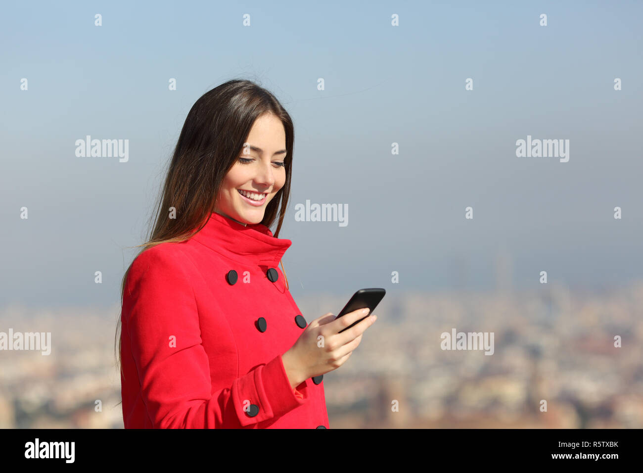 Felice di indossare giacca rossa in inverno utilizzando smart phone all'aperto Foto Stock